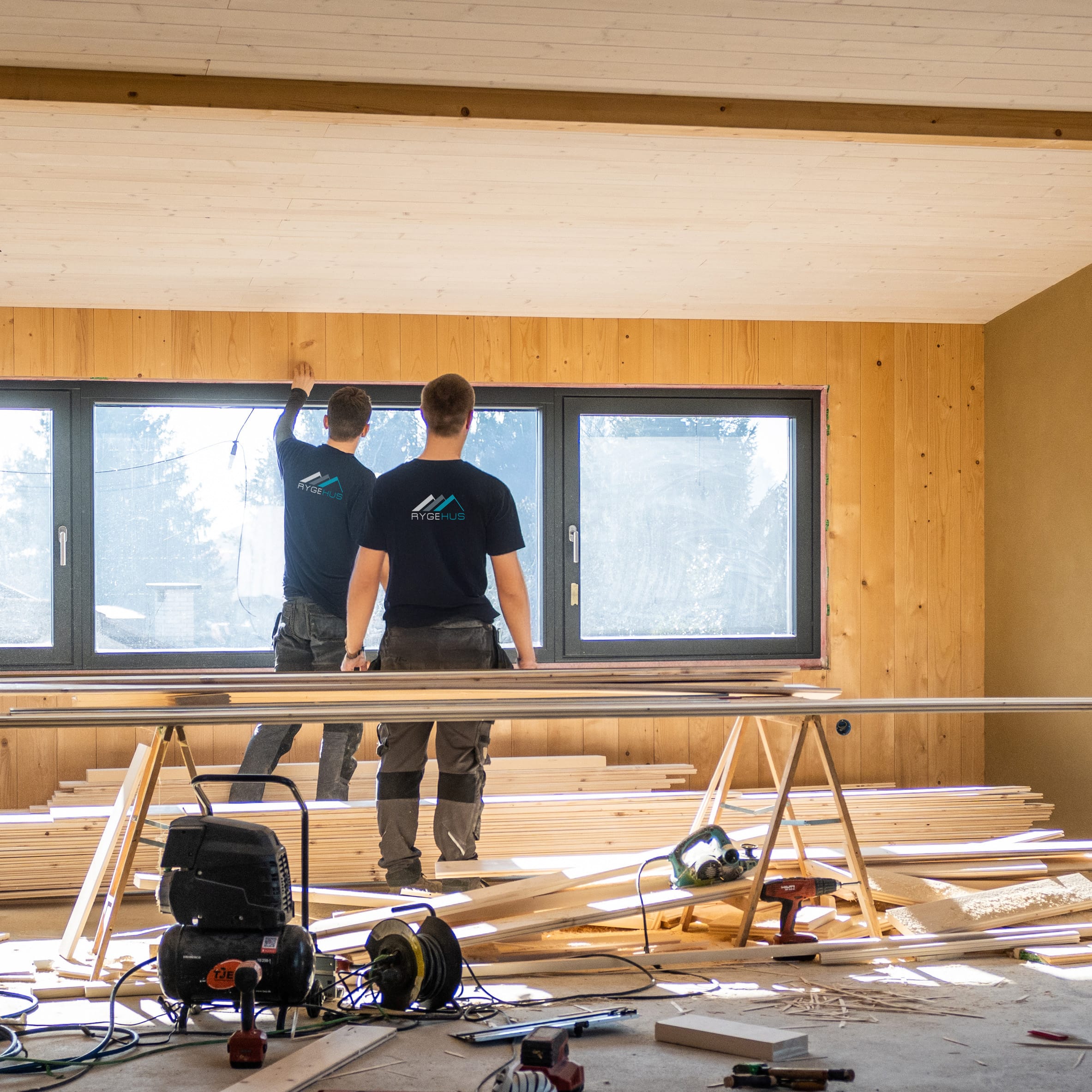 Back view of workers making wooden lining of wall around window. Building new modern house and working on construction site concept.